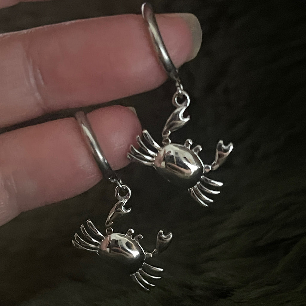 Silver hoop earrings with a crab crab held by a hand against a dark fur background 
