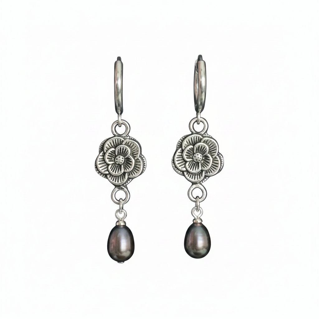 A pair of silver-toned drop earrings featuring an engraved floral pendant and a dangling teardrop-shaped dark pearl, shown against a plain white background.