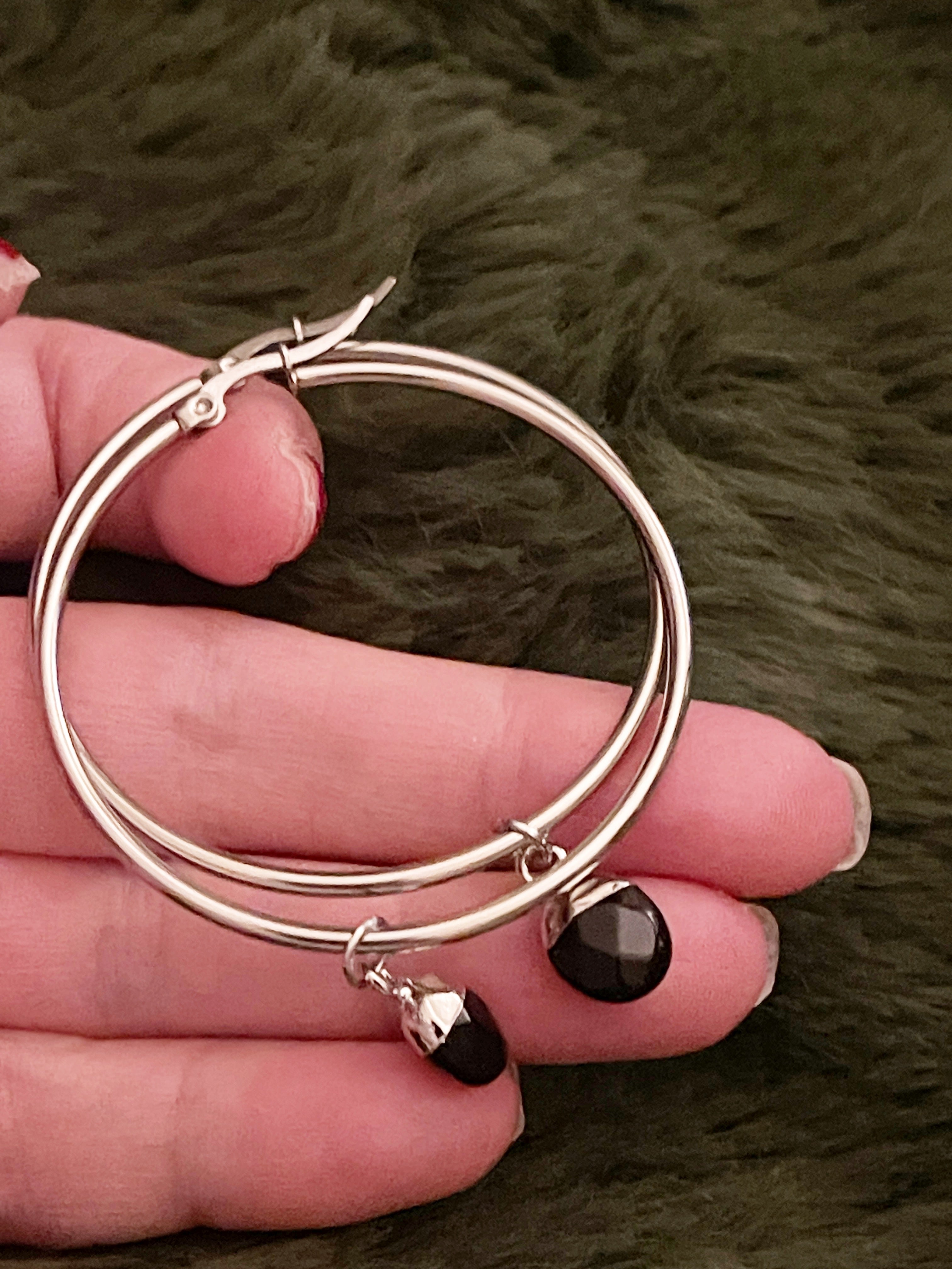 Silver hoop earrings with a black crystal charm held in a hand against a  fur background