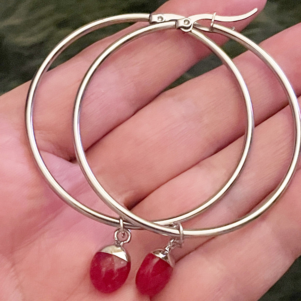 Silver hoop earrings with red gemstone drops held in a hand.