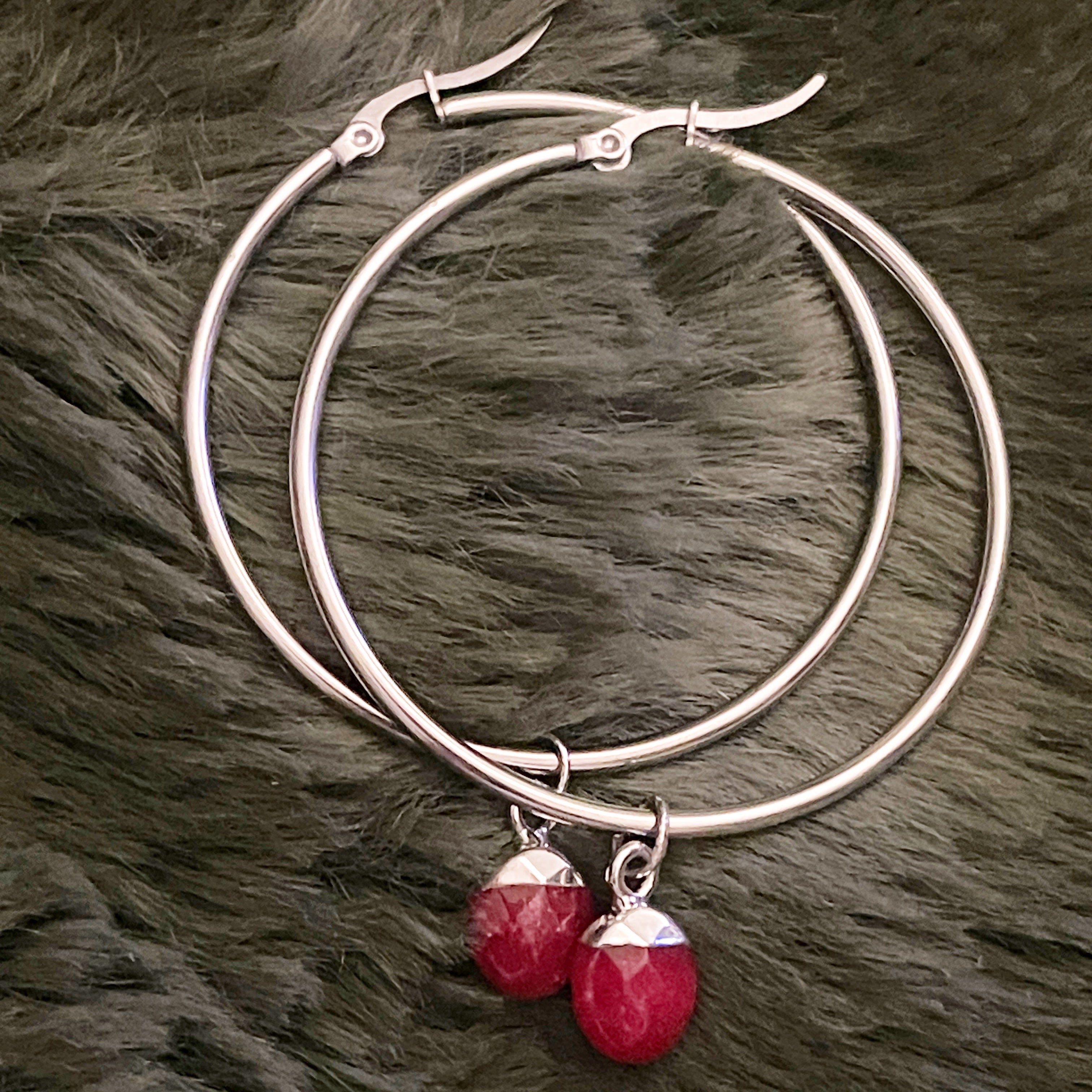 Silver hoop earrings with red gemstone charms on a fur surface