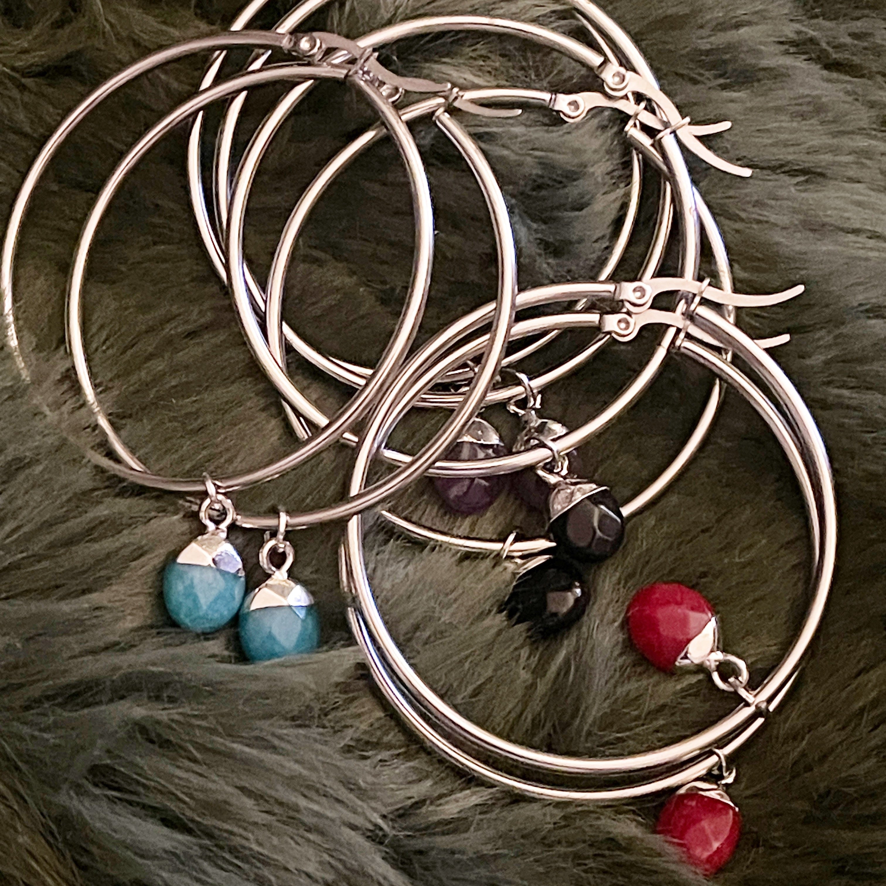 Set of silver hoop earrings with colourful crystals on a fur surface