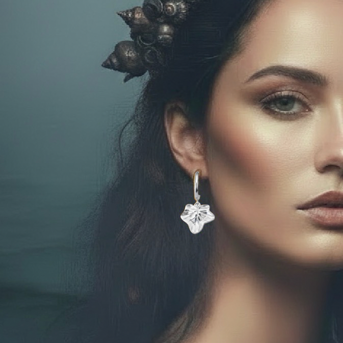 A close-up portrait of a woman wearing a dangling earring. The earring appears to be a silver-toned huggie hoop with a clear faceted flower or shell-like drop.