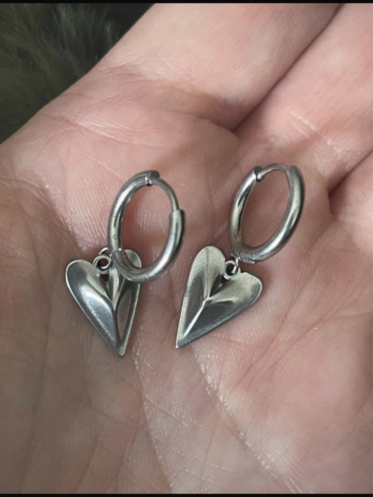 Silver heart-shaped earrings held in a hand.
