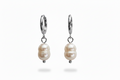 A pair of silver hoop earrings with a natural pearl drop charm, shown against a plain white background.