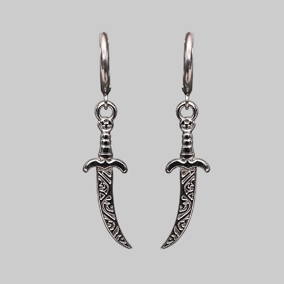 Silver dagger-shaped earrings on a light gray background