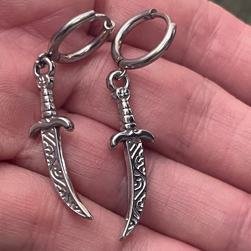 Silver sword-shaped earrings held in a hand.