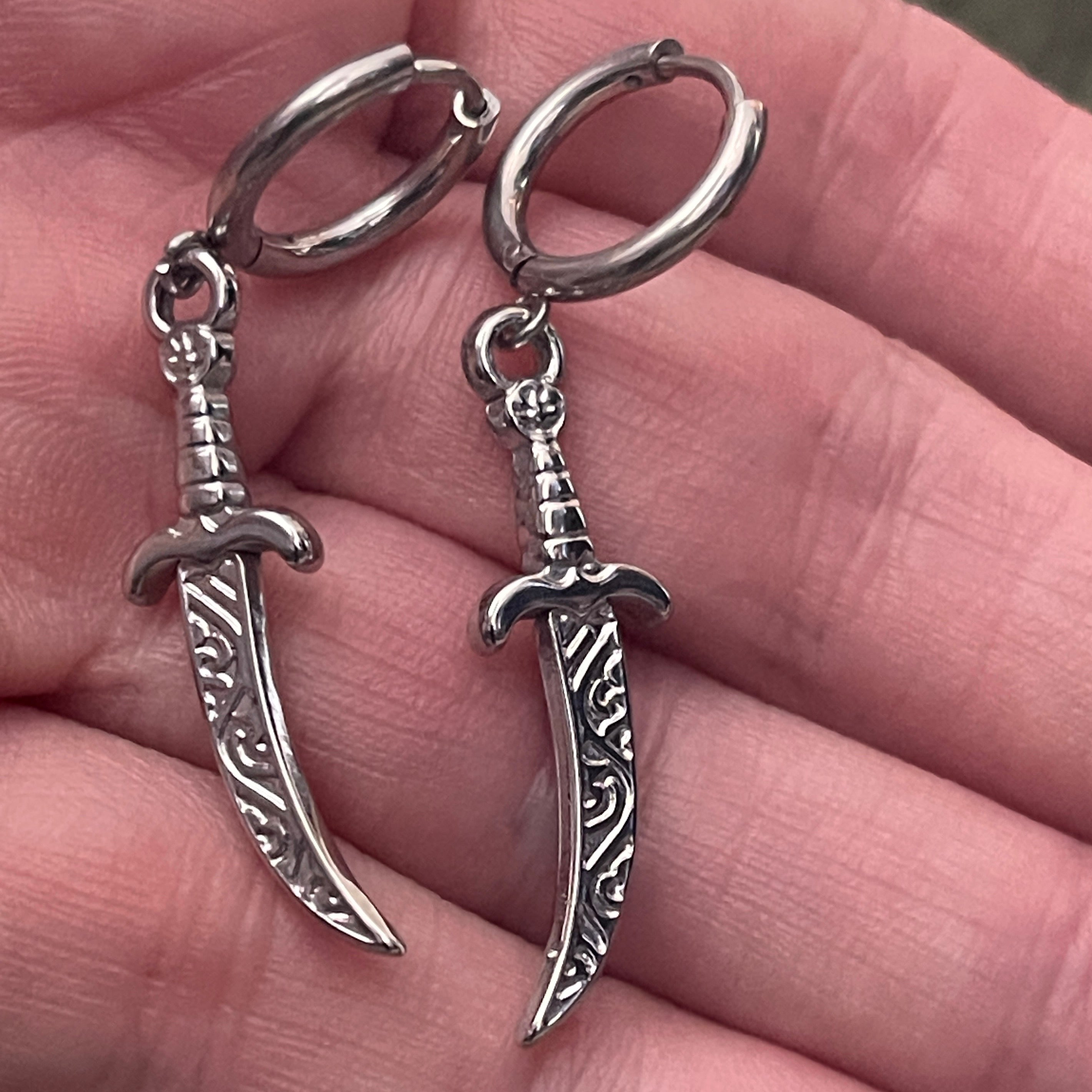 Silver sword-shaped earrings held in a hand.