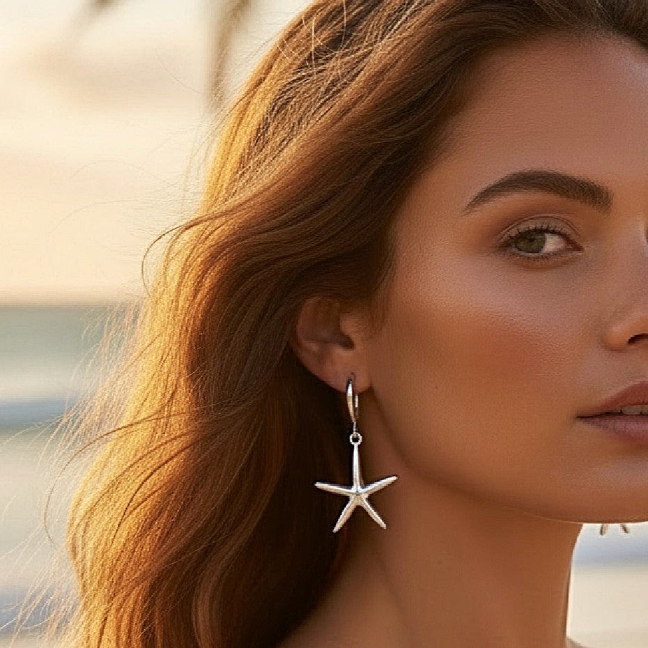 Close-up of a woman wearing starfish earrings with a blurred beach background