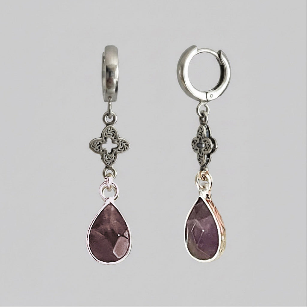 Pair of silver earrings with purple teardrop-shaped stones on a gray background
