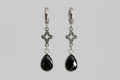 A pair of silver huggie hoop earrings with ornate filigree clover charms and faceted black teardrop gemstones, shown against a solid gray background.