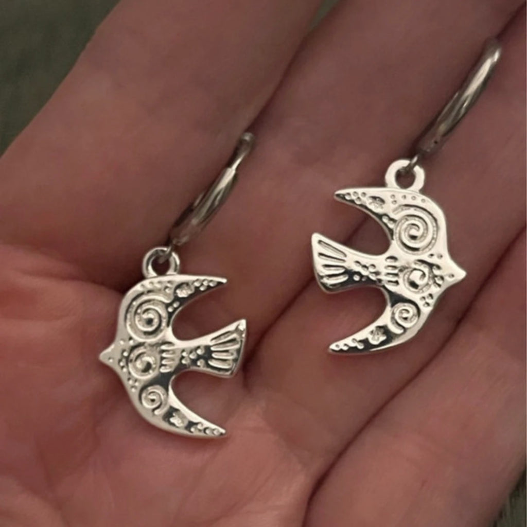 Silver bird-shaped earrings held in a hand