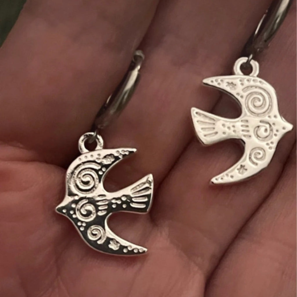 Silver fish-shaped earrings held in a hand.