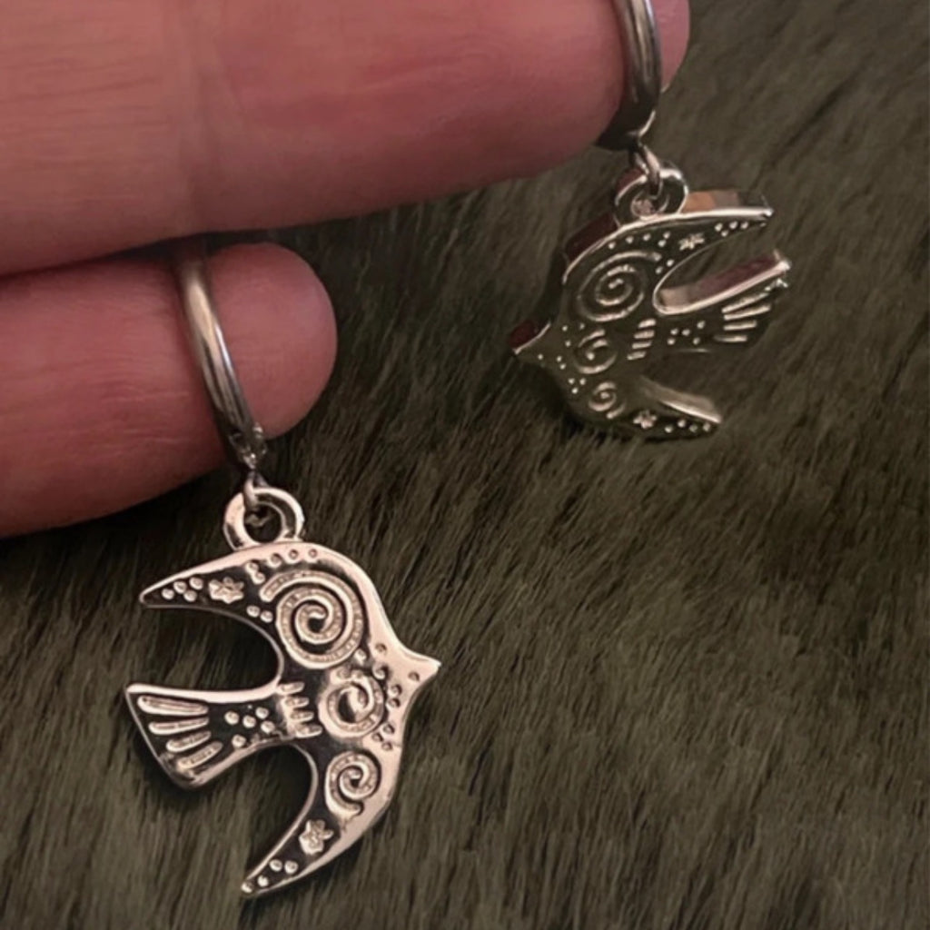 Silver bird-shaped earrings held by a hand on a textured surface