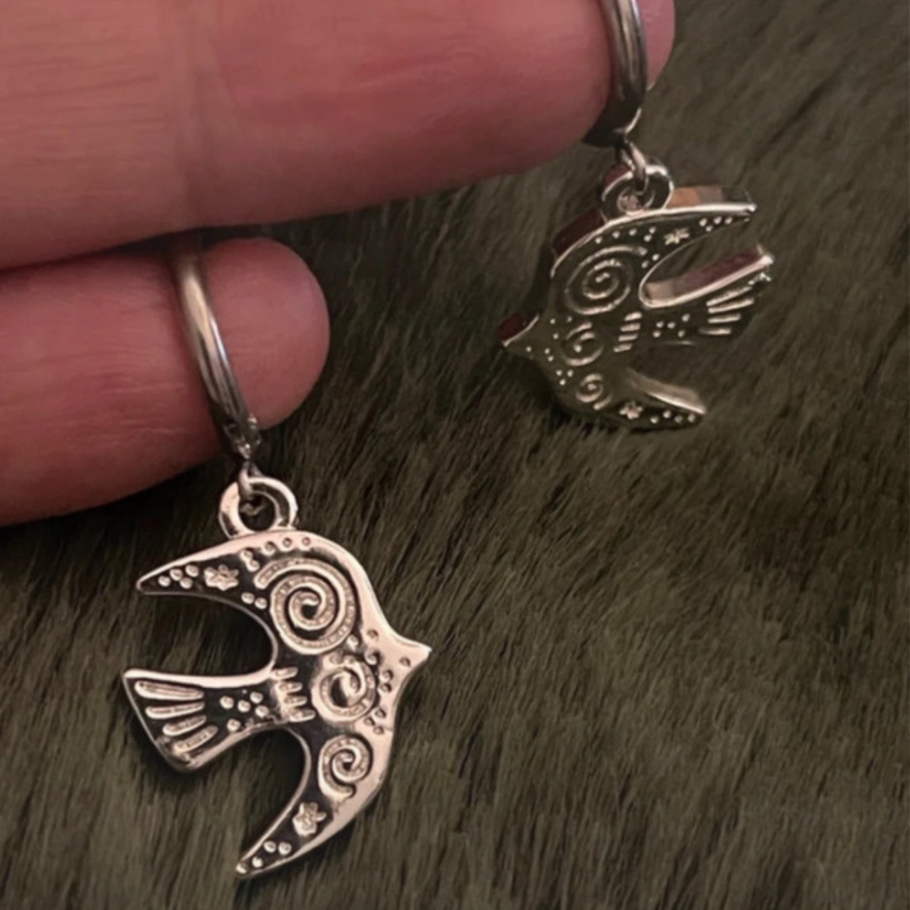 Silver bird-shaped earrings held by a hand on a textured surface