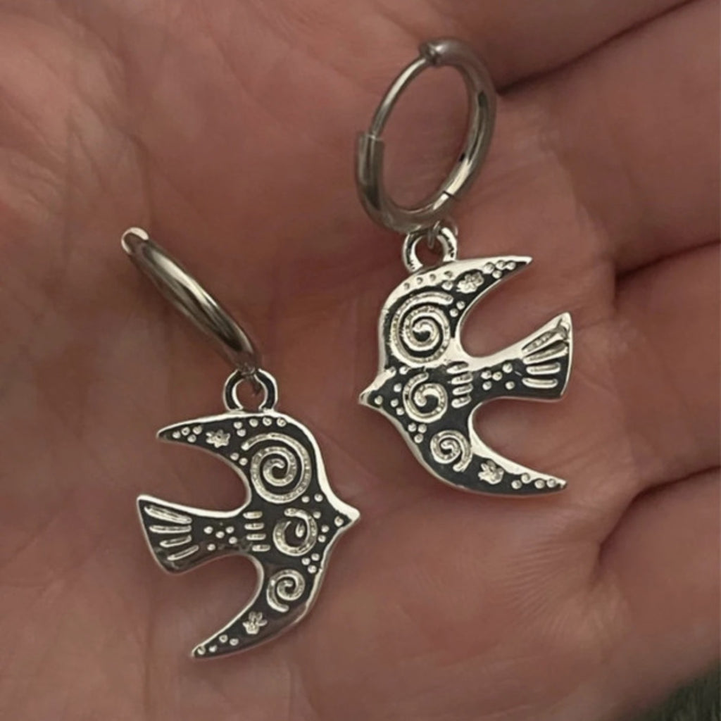 Silver bird-shaped earrings held in a hand.