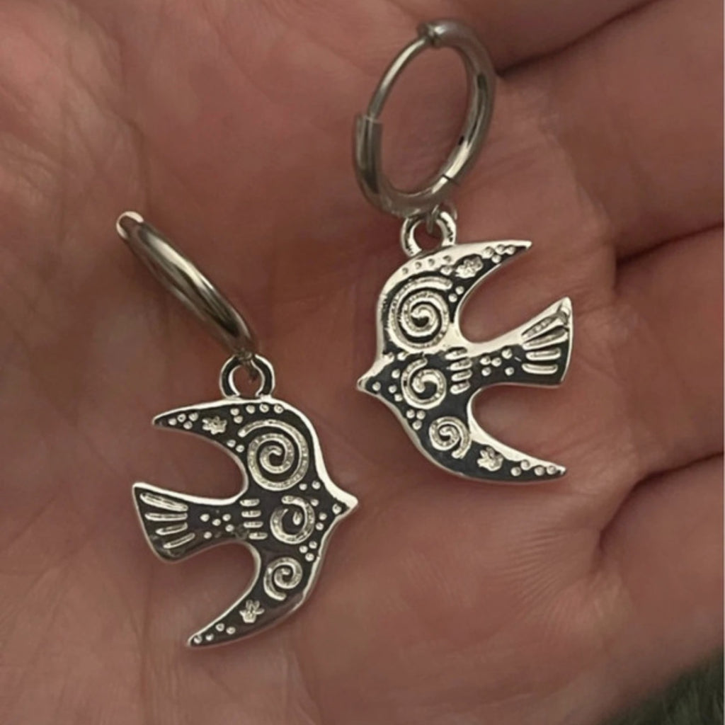 Silver bird-shaped earrings held in a hand