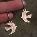 Silver bird-shaped earrings held between fingers on a textured surface