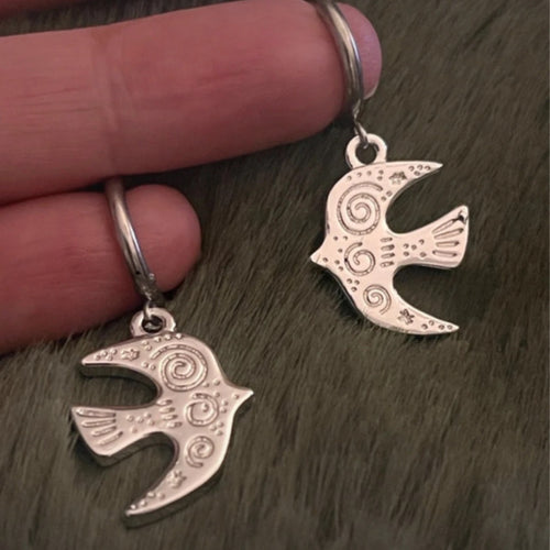 Silver bird-shaped earrings held between fingers on a textured surface