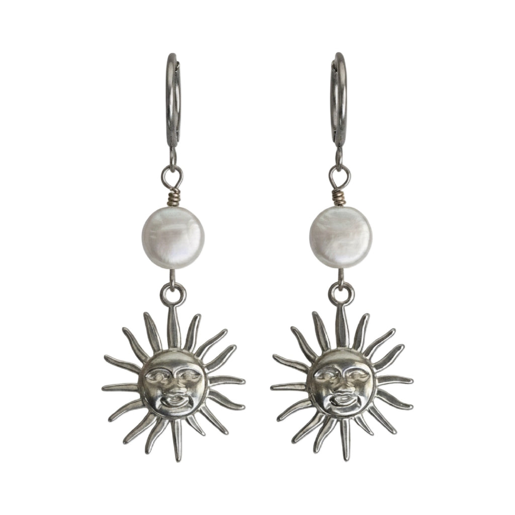 A pair of silver drop earrings featuring a round white pearl and a dangling sun face charm, shown against a plain white background.