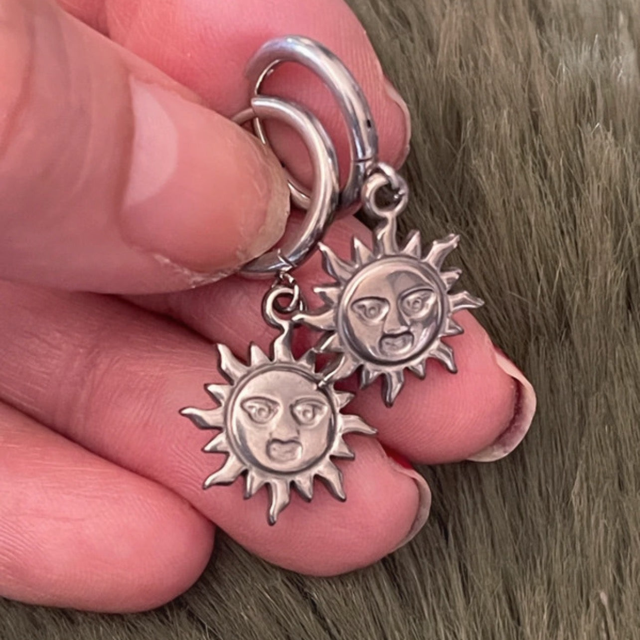 Silver sun and moon earrings held between fingers against a brown background