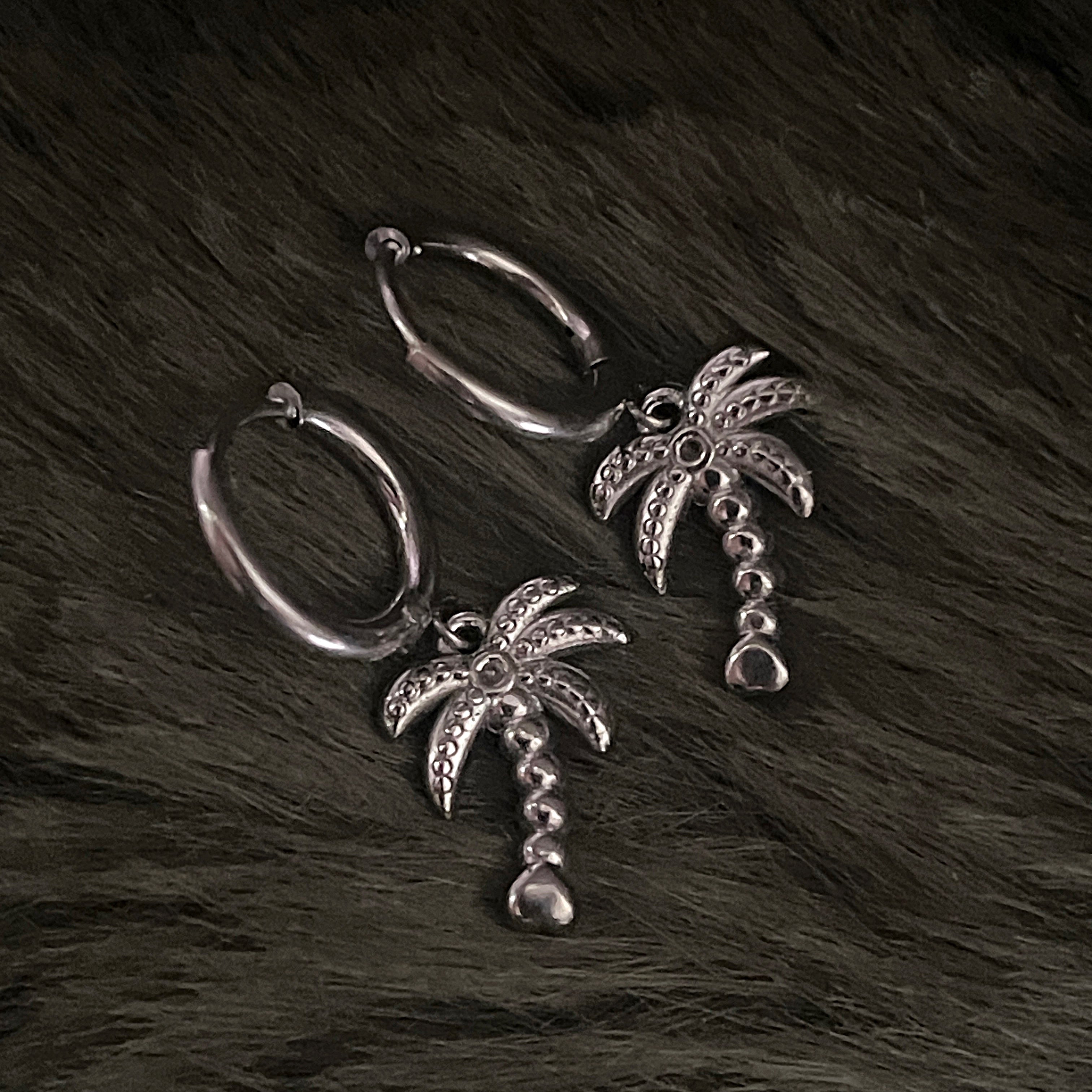 Silver earrings with palm tree charms on a fur background 
