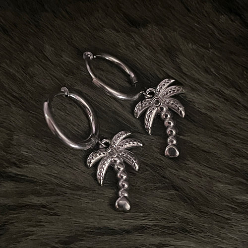 Silver earrings with palm tree charms on a fur background 