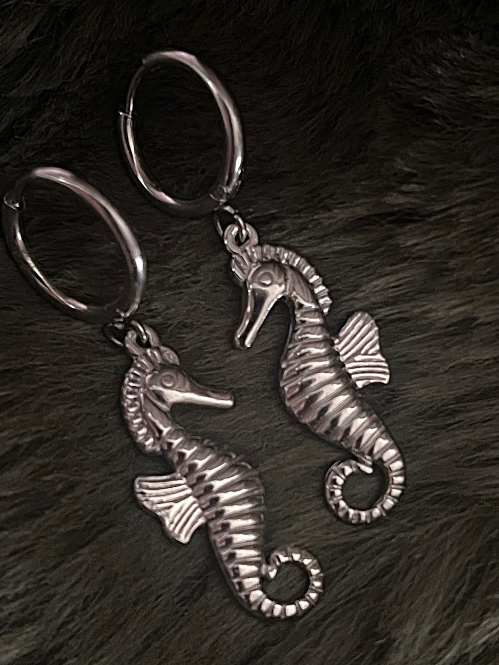 Two silver seahorse earrings on a dark textured surface