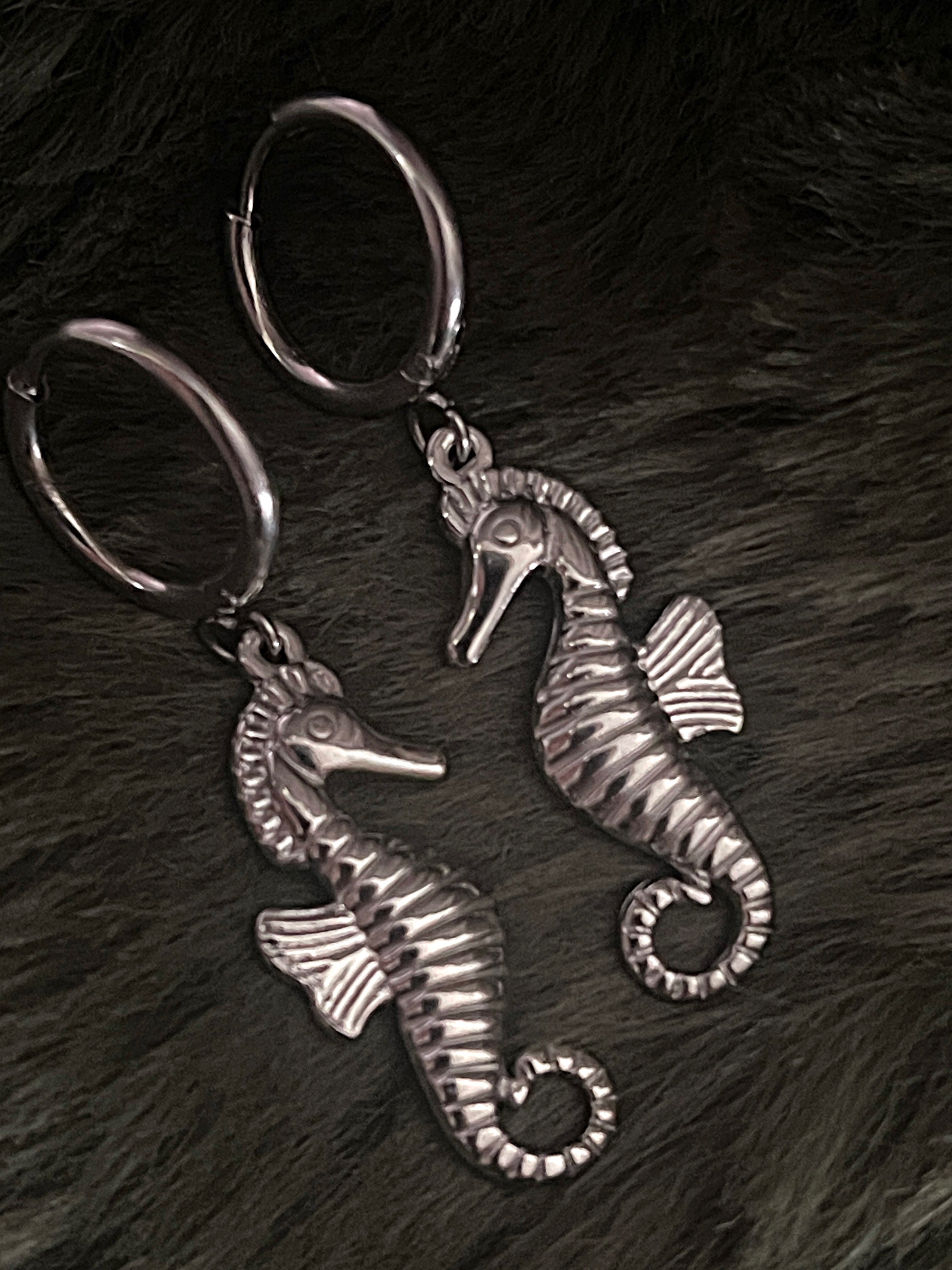 Two silver seahorse earrings on a dark textured surface