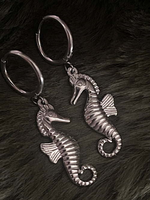Two silver seahorse earrings on a dark textured surface