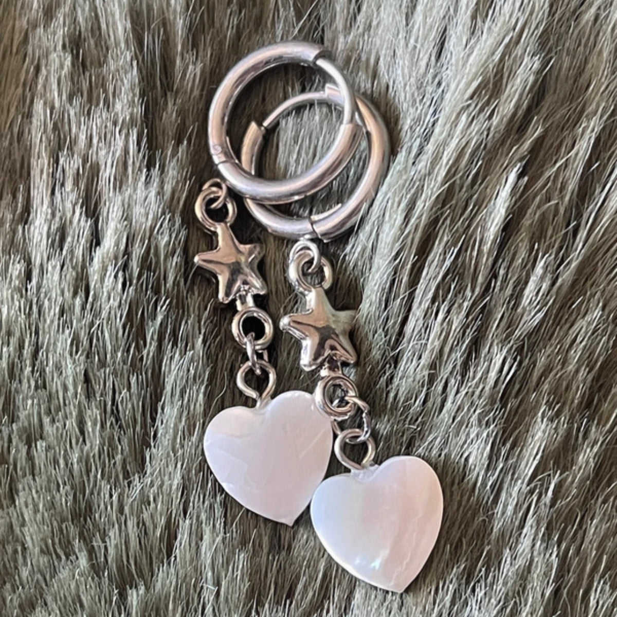 Silver earrings with heart and star charms on a fur background