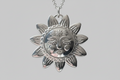 Silver sun-shaped pendant with face design on a gray background