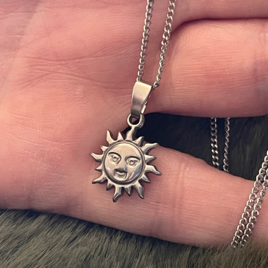 Silver sun-shaped pendant necklace on a finger against a neutral background