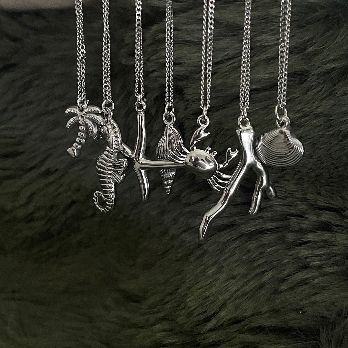 Collection of silver necklaces with various pendants on a dark textured background