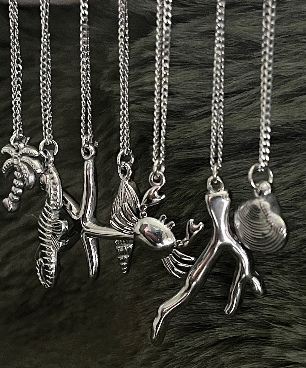Collection of silver necklaces with various pendants on a dark fur background