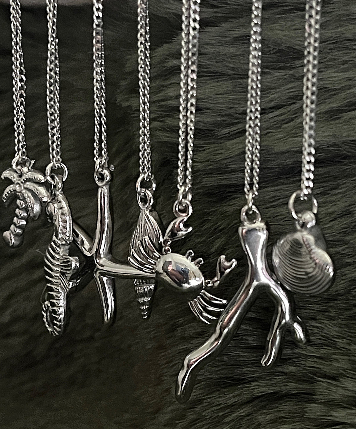 Collection of silver necklaces with various pendants on a dark fur background