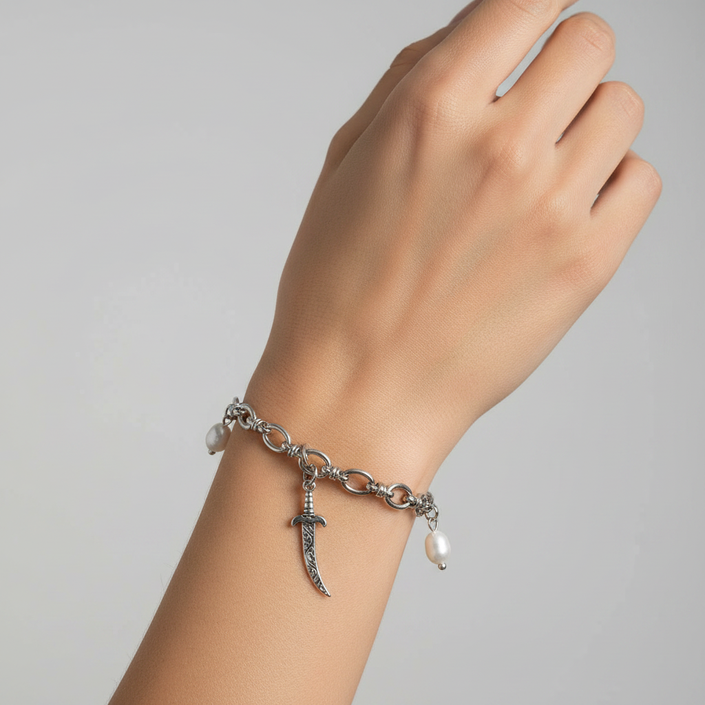 A wrist showing a silver sword and pearl bracelet against a grey background 