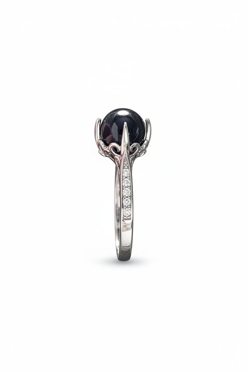 A silver ring featuring a large, round black gemstone in a claw setting, with a pavé band of small clear stones, shown against a plain white background.