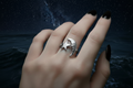 Silver ring with moon and star design on a hand against a dark background