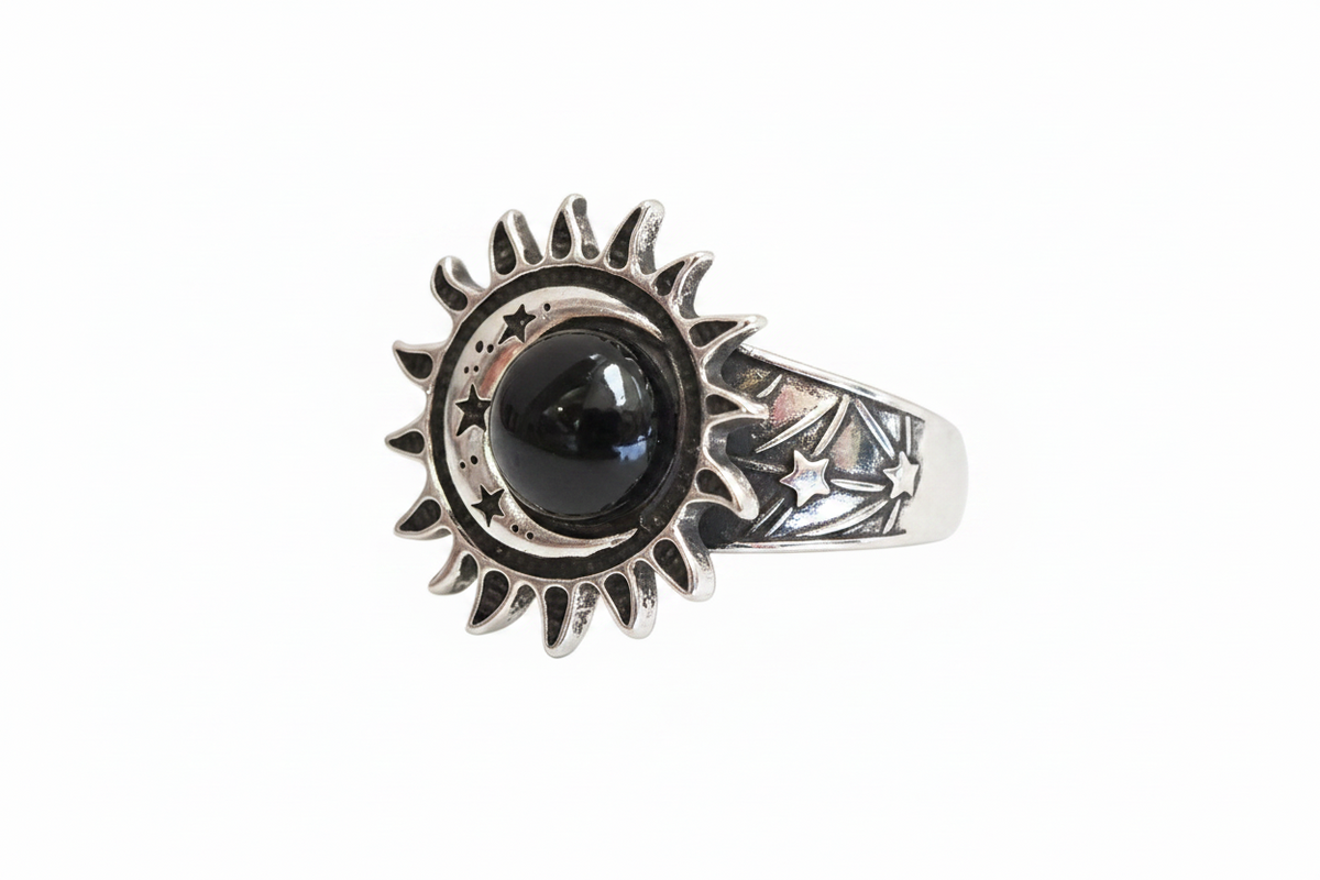 A silver ring featuring a sunburst and moon design with a central black round stone and star details on the band, shown against a plain white background.