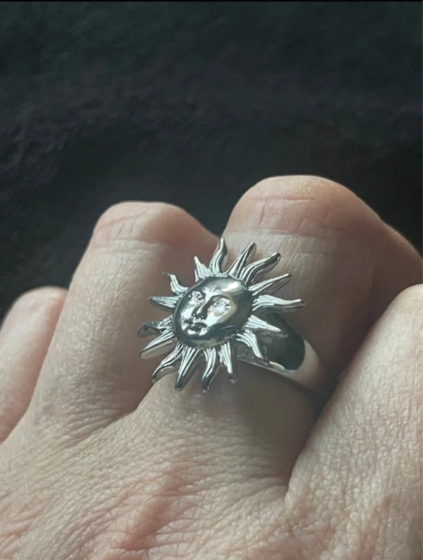 Silver sun-shaped ring with face design on a finger against a dark background