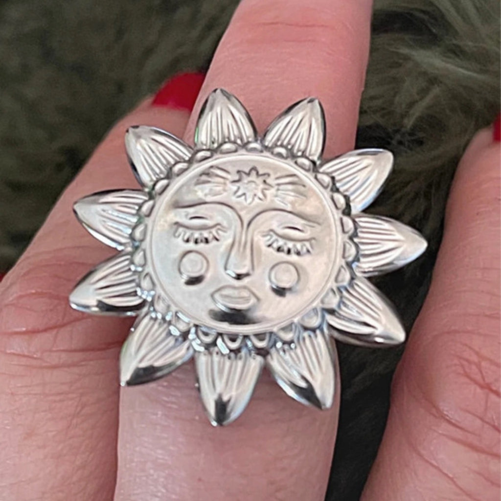Silver sun-shaped ring with face design on a finger
