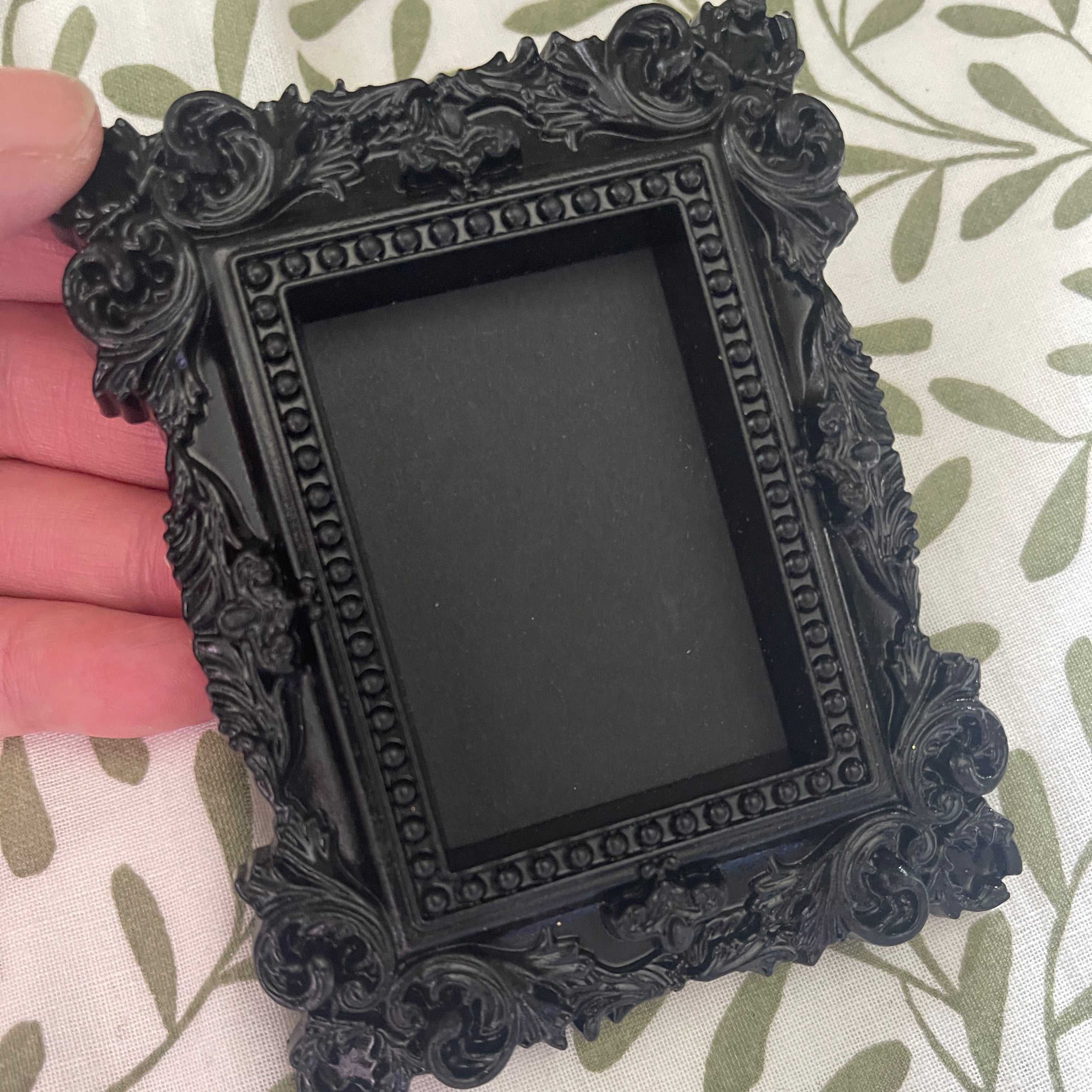 Decorative black picture frame held by a hand on a patterned fabric background