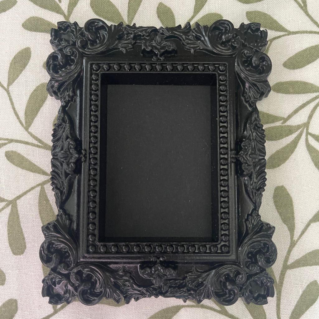Decorative black picture frame with intricate designs on a leaf-patterned background