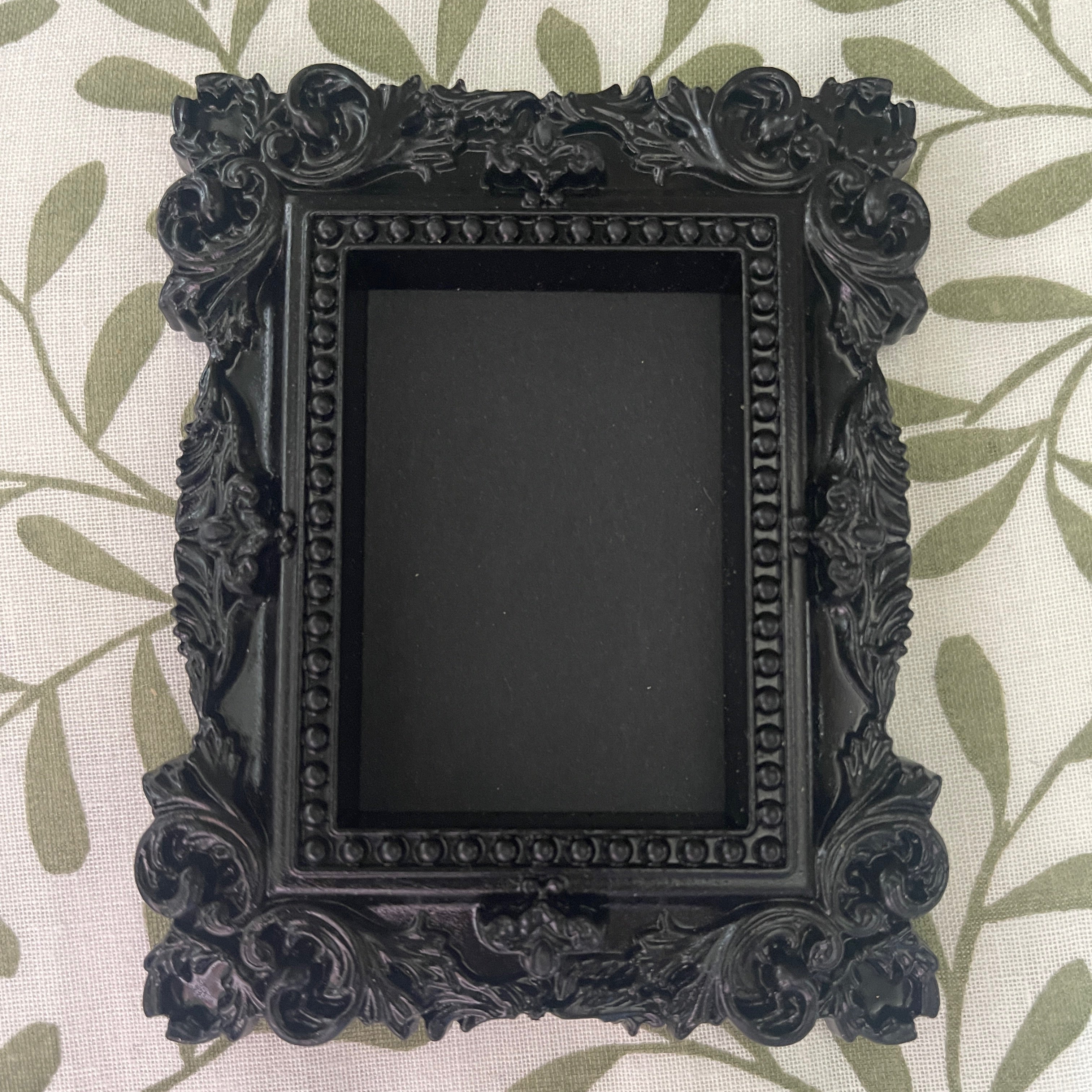 Decorative black picture frame with intricate designs on a leaf-patterned background