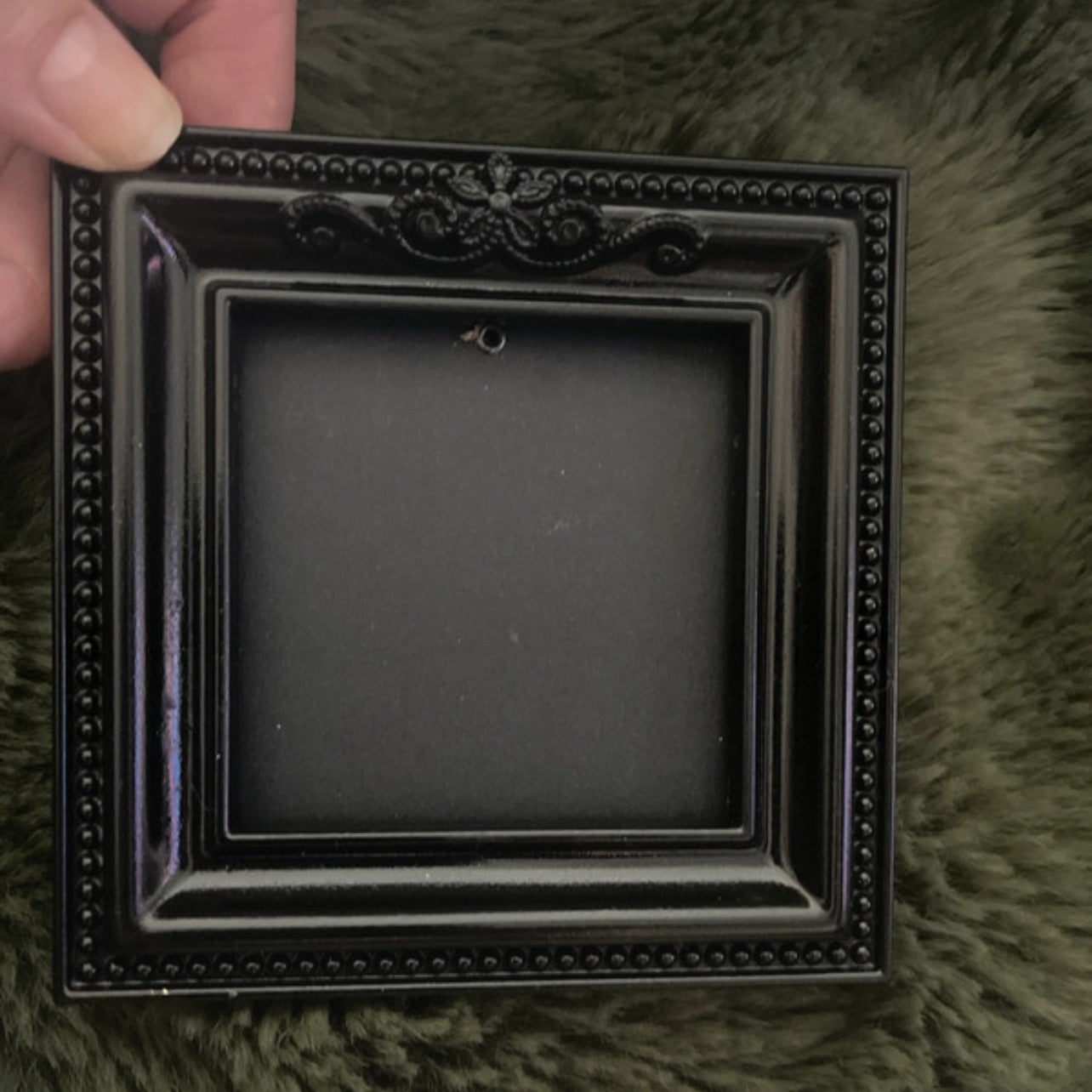 Black decorative frame held by a hand on a green textured surface