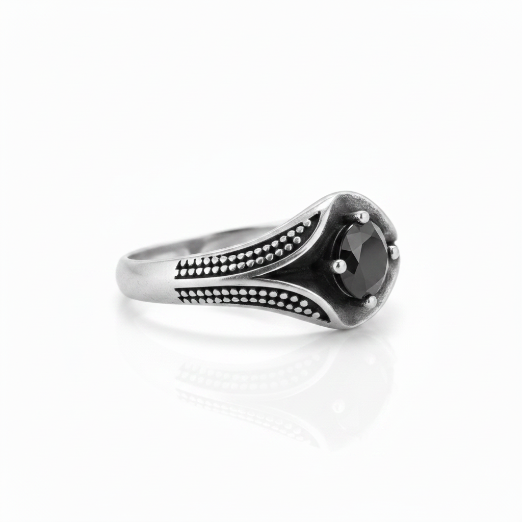 A silver-toned ring with a curved, textured band and a central round black gemstone, photographed on a clean white background with a soft reflection below.