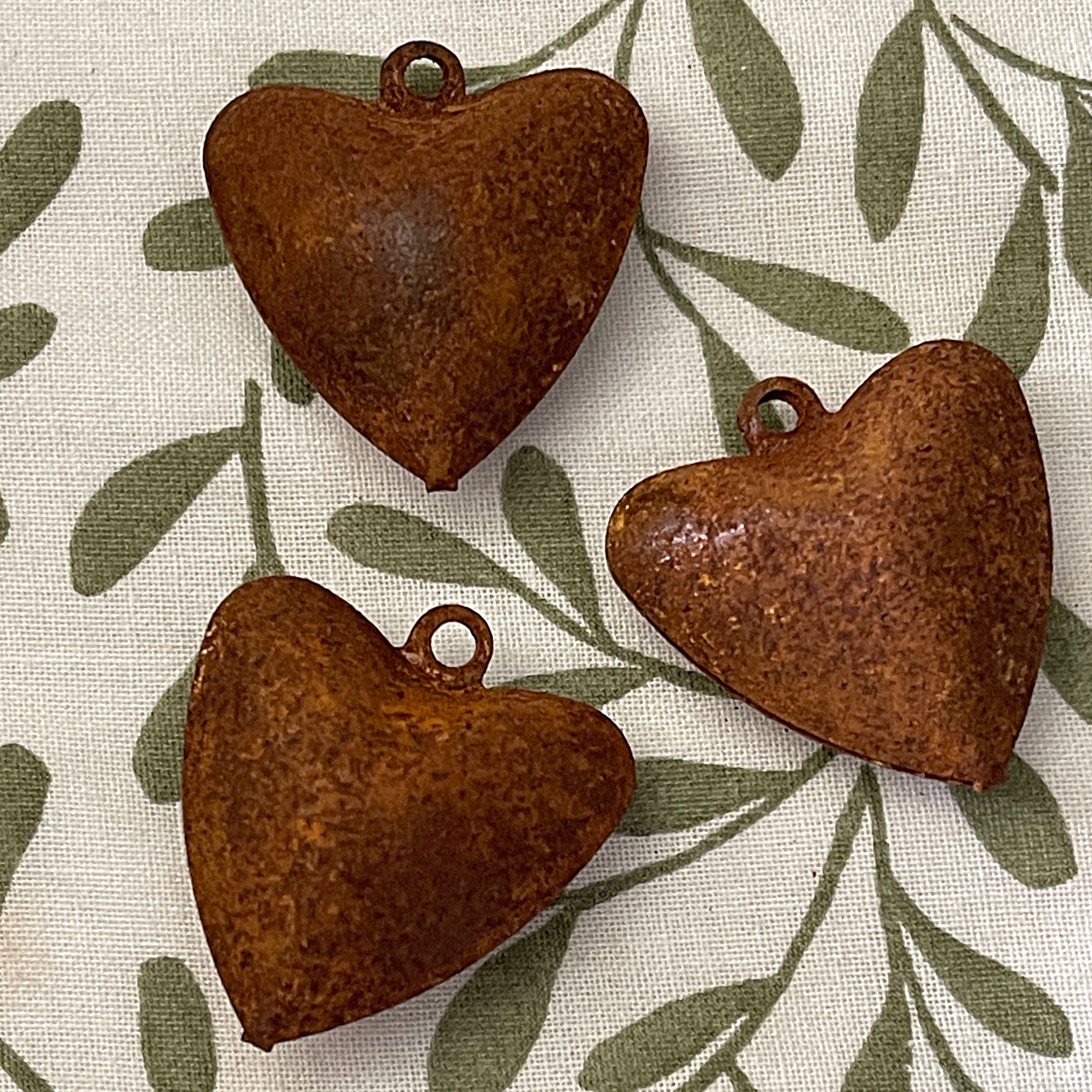 Three rusted heart-shaped metal bells on a fabric background with leaf pattern