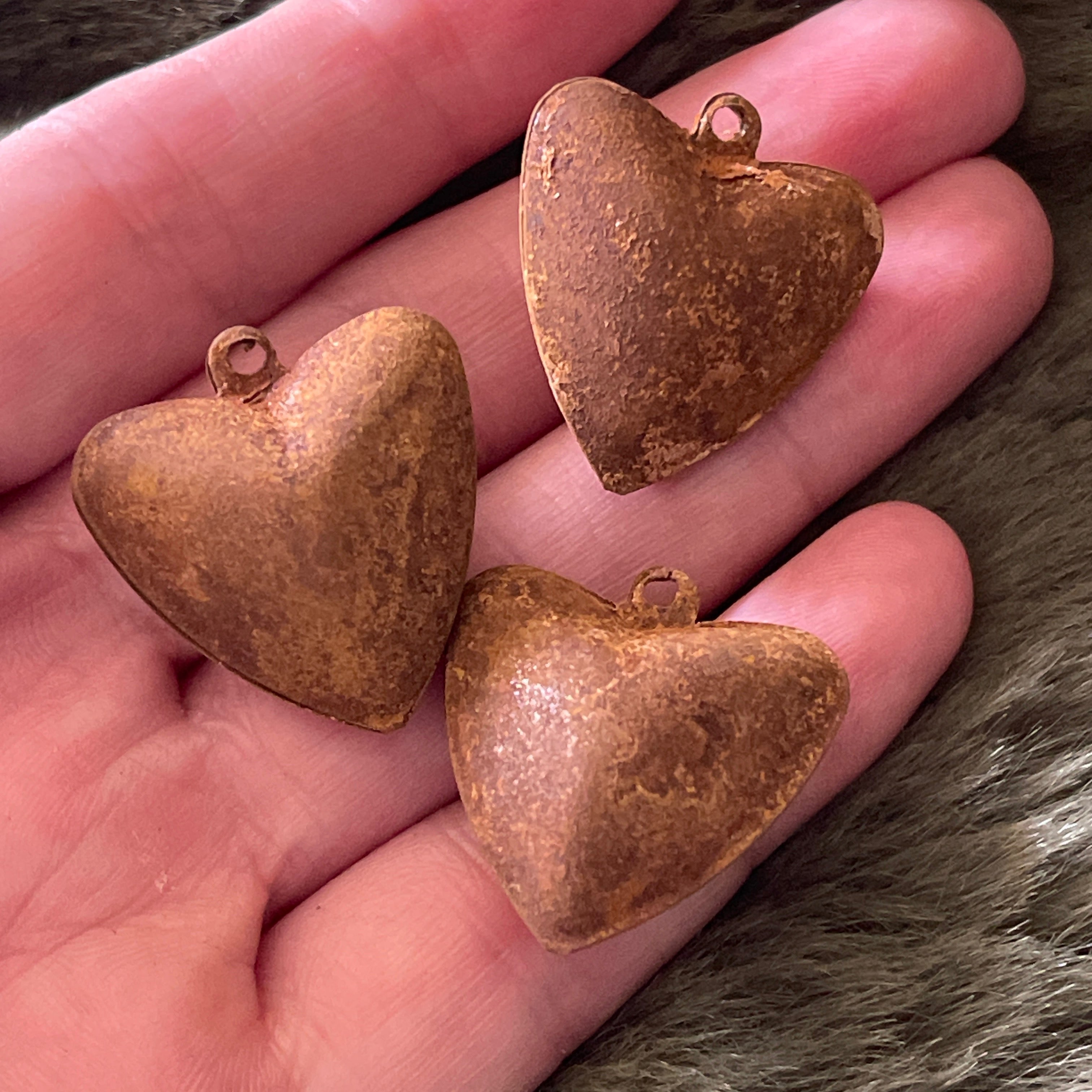 Three rusted heart-shaped metal pendants on a hand.