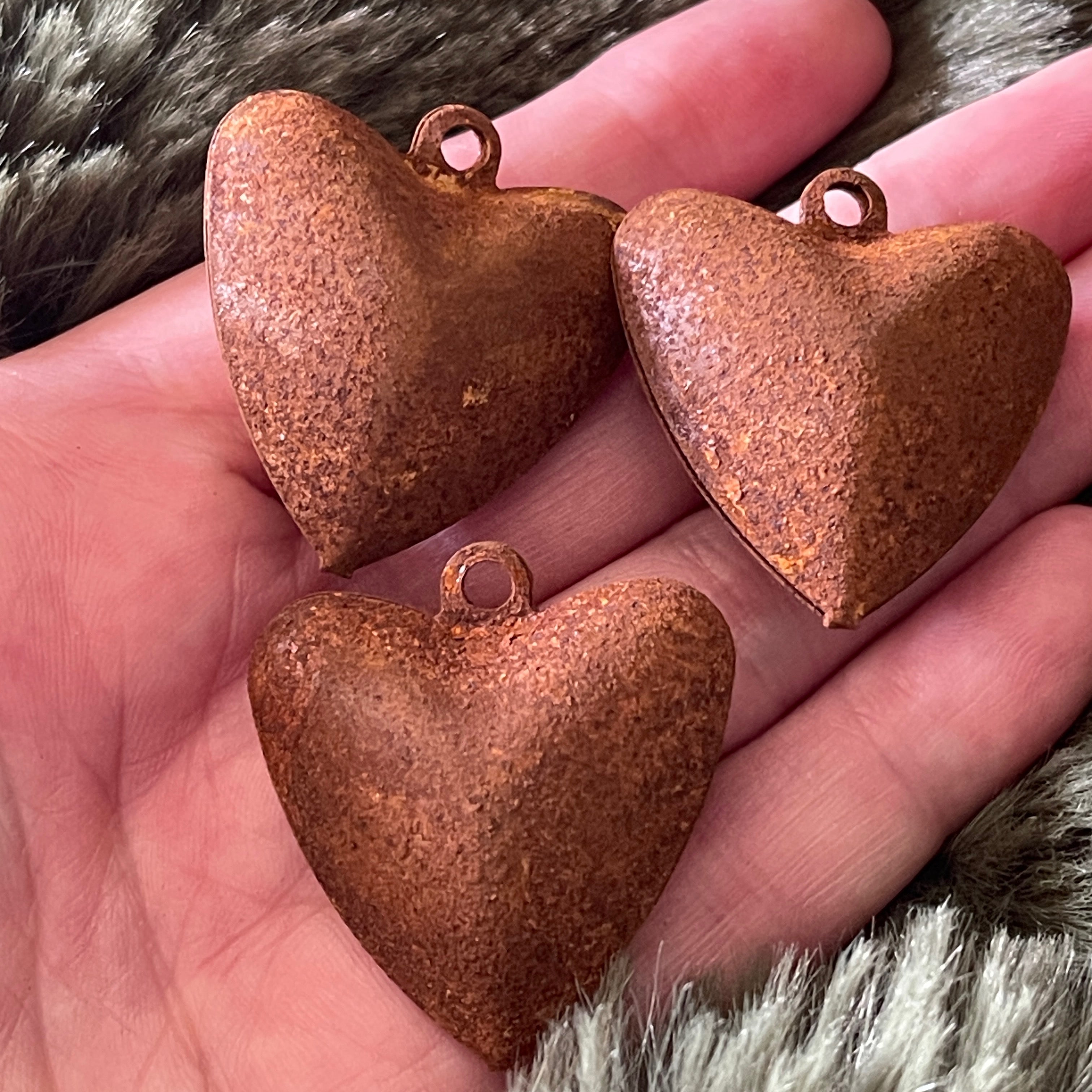 Three rusted heart-shaped metal bells held in a hand with fur background.